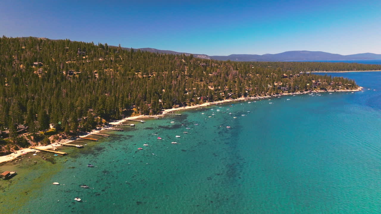 Beautiful azure water of Lake Tahoe with many boats on. Green pine trees overgrowing the rocky shore. View from top.