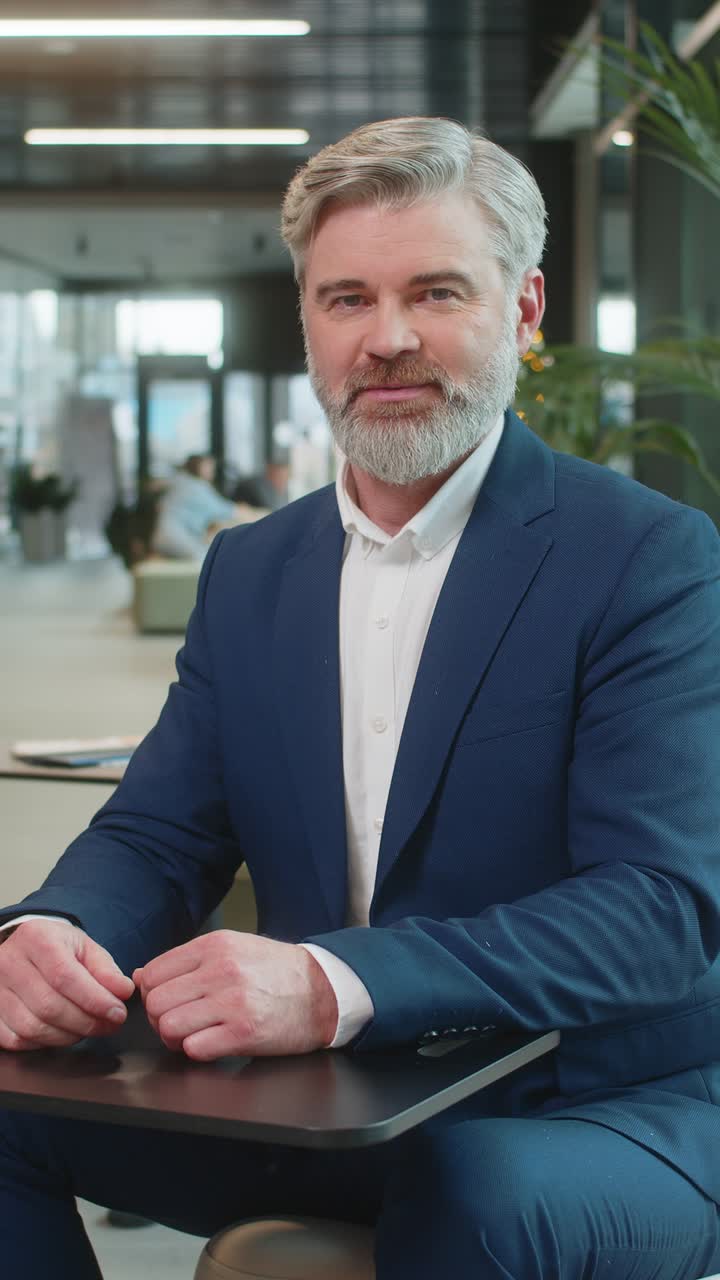 Happy middleaged caucasian businessman looking at camera and waving hand hello in office lobby