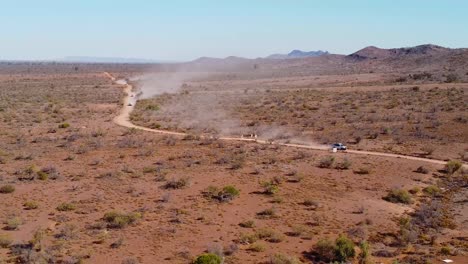 four wheel drive vehicles speed down a dusty dirt road, leaving a trail of dust in their wake