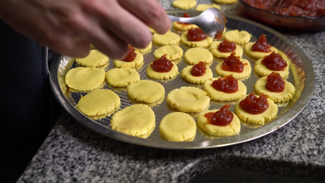 manos poniendo relleno de pasta de membrillo encima de la masa para galletas antes de hornear