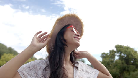 Feliz-Adolescente-Birracial-Con-Sombrero-Y-Gafas-De-Sol-Sonriendo-En-Un-Jardín-Soleado,-Cámara-Lenta