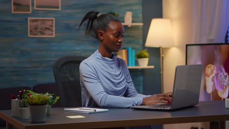 Black woman typing on computer smiling late at night