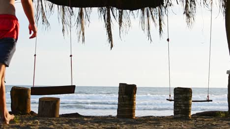 joven caminando hacia luego tomando asiento en un columpio frente al mar en costa rica