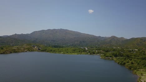 Vista-Aérea-De-La-Costa-Del-Lago-En-Verano-Con-Montaña-Verde-Detrás-En-San-Luis,-Argentina