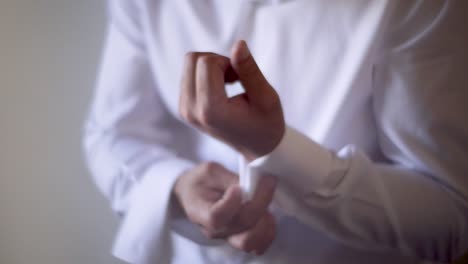 a man finishing dressing himself in a formal attire, buttoning up his shirt