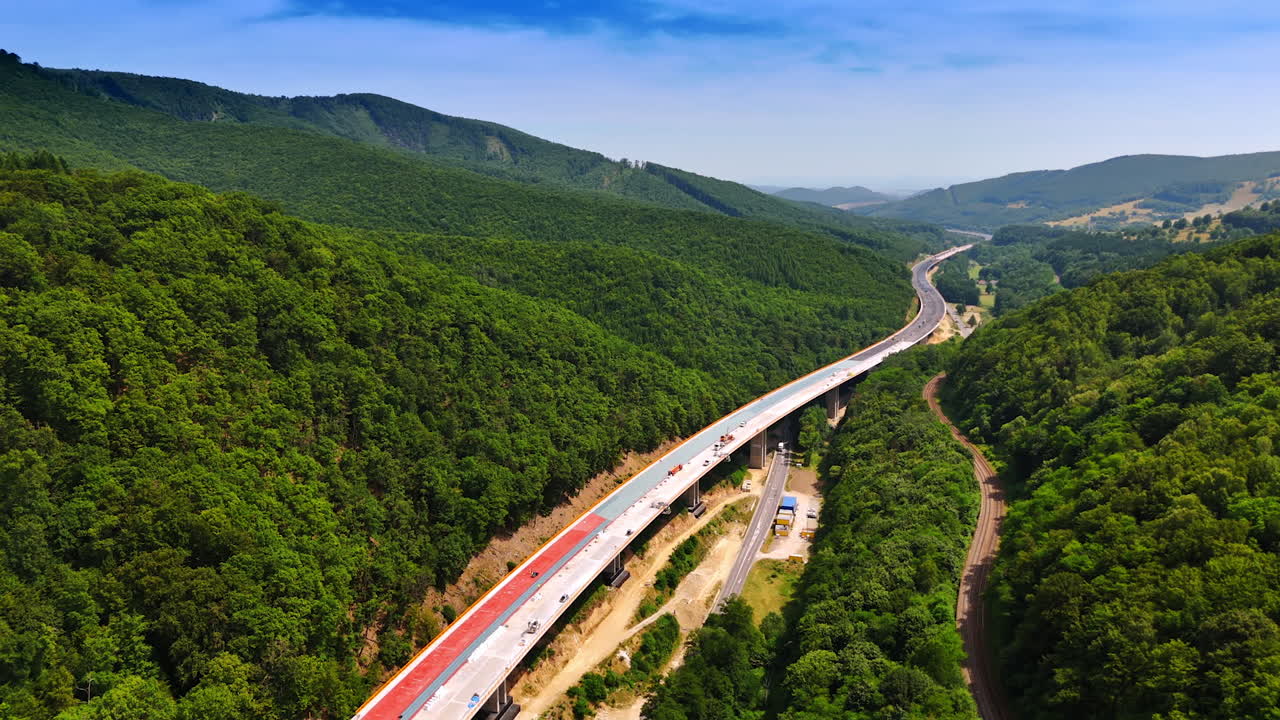 Long freeway is being built along the spectacular mountains. Drone footage above the road construction
