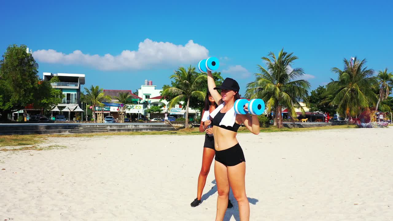 Athletic girls exercise on colorful tropical landscape with white sandy beach and palm trees near vacations resort on a sunny day in Thailand