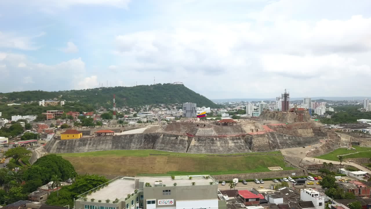 Panoramica aerea verso destra su un'antica fortezza in pietra circondata da quartieri urbani e dal moderno skyline della città alla luce del giorno