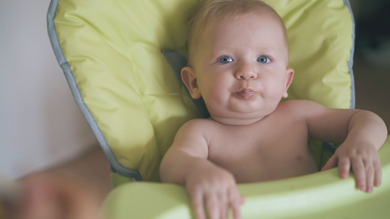 la mamá alimenta al bebé con sopa de crema en una silla alta verde suave