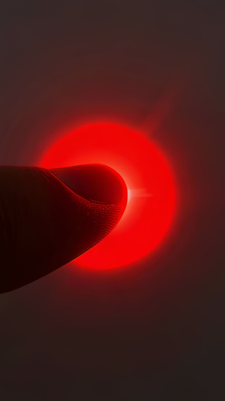 Vertical video: Pressing fingertip covering red LED in close-up, revealing crescent halo and flare