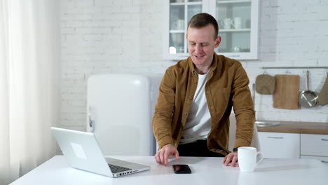 young businessman working at home during quarantine. happy male freelancer using laptop in his job in the kitchen. student studying in a flat.