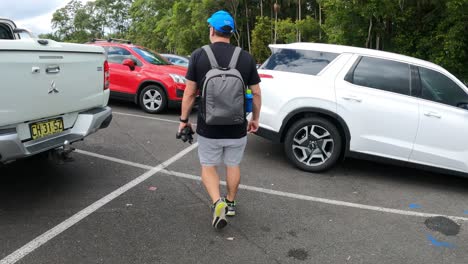 a man walks past various parked cars in a lot