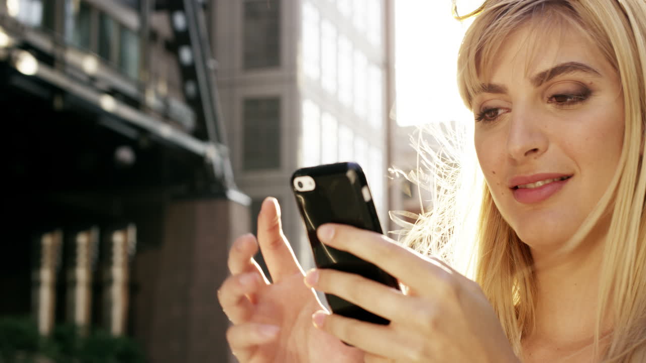 Bella donna bionda che usa lo smartphone, con un bagliore di luce solare.