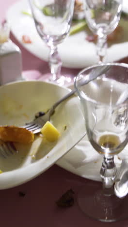 dirty plates and cutlery with wineglasses are located on a pink tablecloth. camera motion forward vertical video