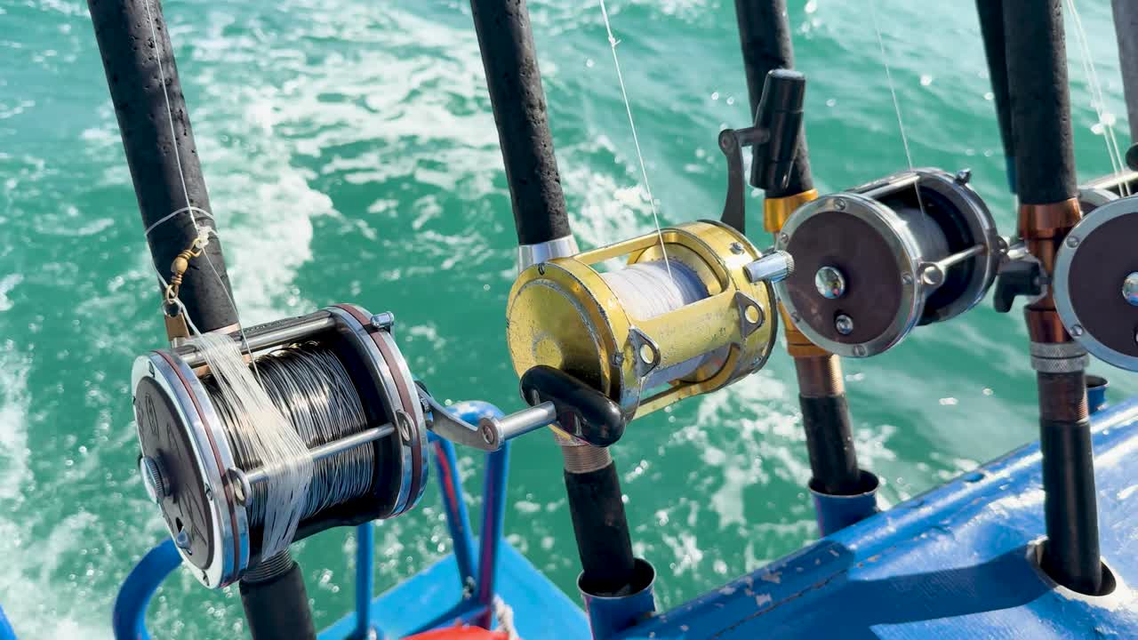 Fishing rods secured on a boat in Phuket, Thailand, with ocean waves in the background. Bright daylight enhances the scene