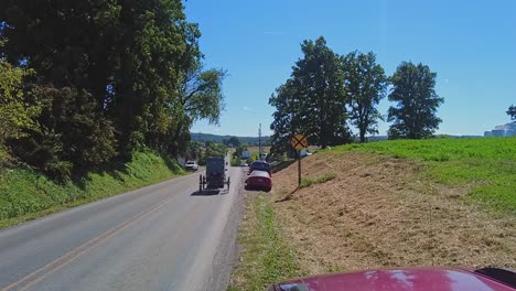 an amish horse and buggy passing down a country, with amish teens, in slow-motion on a beautiful sunny day