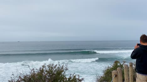 Surfer-Mann-Filmt-Mit-Digitaltelefon-Die-Großen-Wellen-In-Estoril,-Cascais