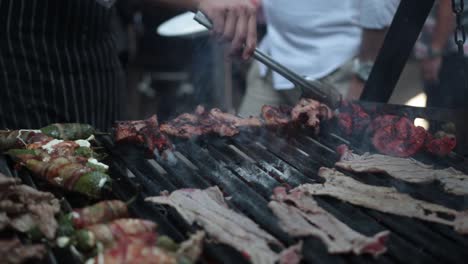 slow motion shot of a street vendor flipping meats on hsi grill with metal tongs
