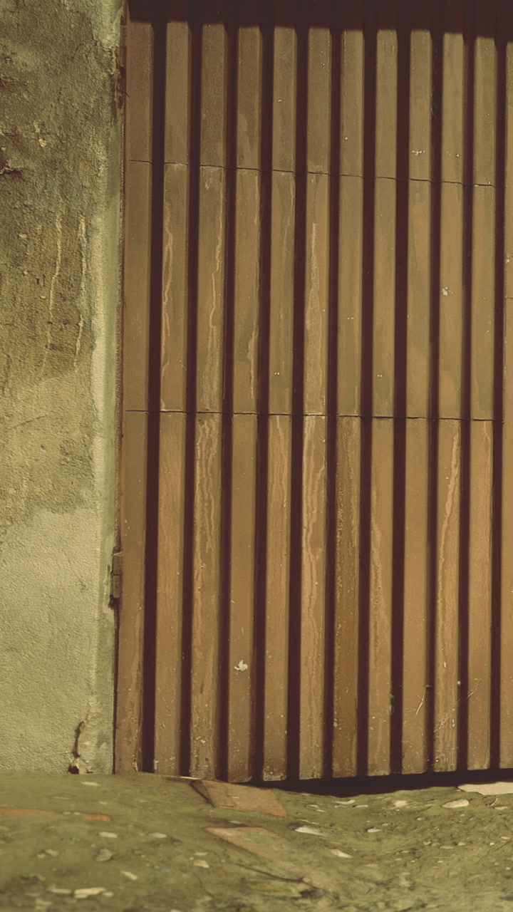 A wooden door made of vertical slats stands against a rough textured wall