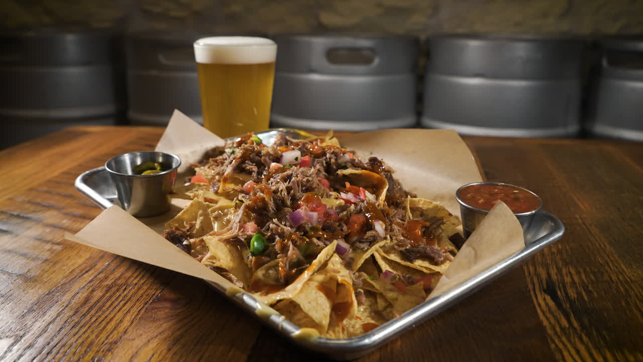 Nachos carnitas da birreria ricoperti di queso abbinati a una birra chiara, slider 4K.