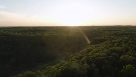 Rising-jib-like-movement-from-behind-the-trees-to-high-altitude-revealing-a-beautiful-sunset-behind-gorgeous-thick-foliage-of-trees-and-small-hills-at-a-campsite-in-Wisconsin,-USA