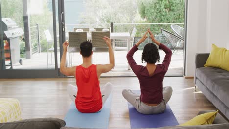 Happy-diverse-male-couple-doing-yoga,-meditating-in-living-room