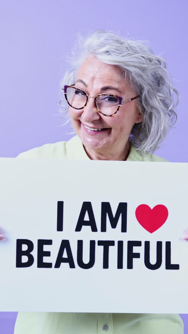 Anziana donna che tiene un cartello 'Sono Bella' e sorride.