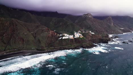 aerial tilt up of remote village on volcanic green coast in tenerife
