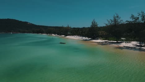 calmly rippling clear waters where an empty boat is bobbing at anchor just off the crisp white sand beach on the island of koh rong sanloem. low angle high speed drone dolley shot