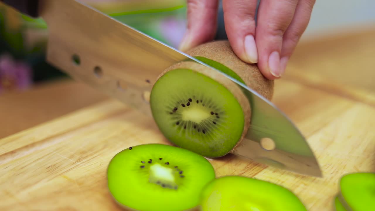 Women's hands Housewives cut with a knife fresh kiwi on the cutting Board of the kitchen table