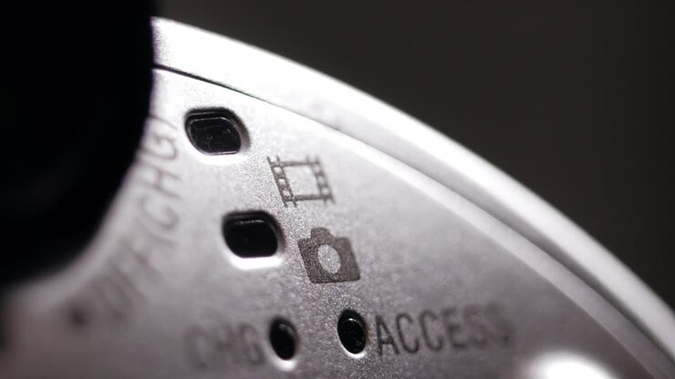 Macro ripresa rotante del corpo di una videocamera argentata che mostra le icone di film e foto e i fori per il LED di accesso