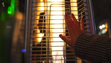 person touching with his hand an outdoor stove that gives off an orange fire flame at night