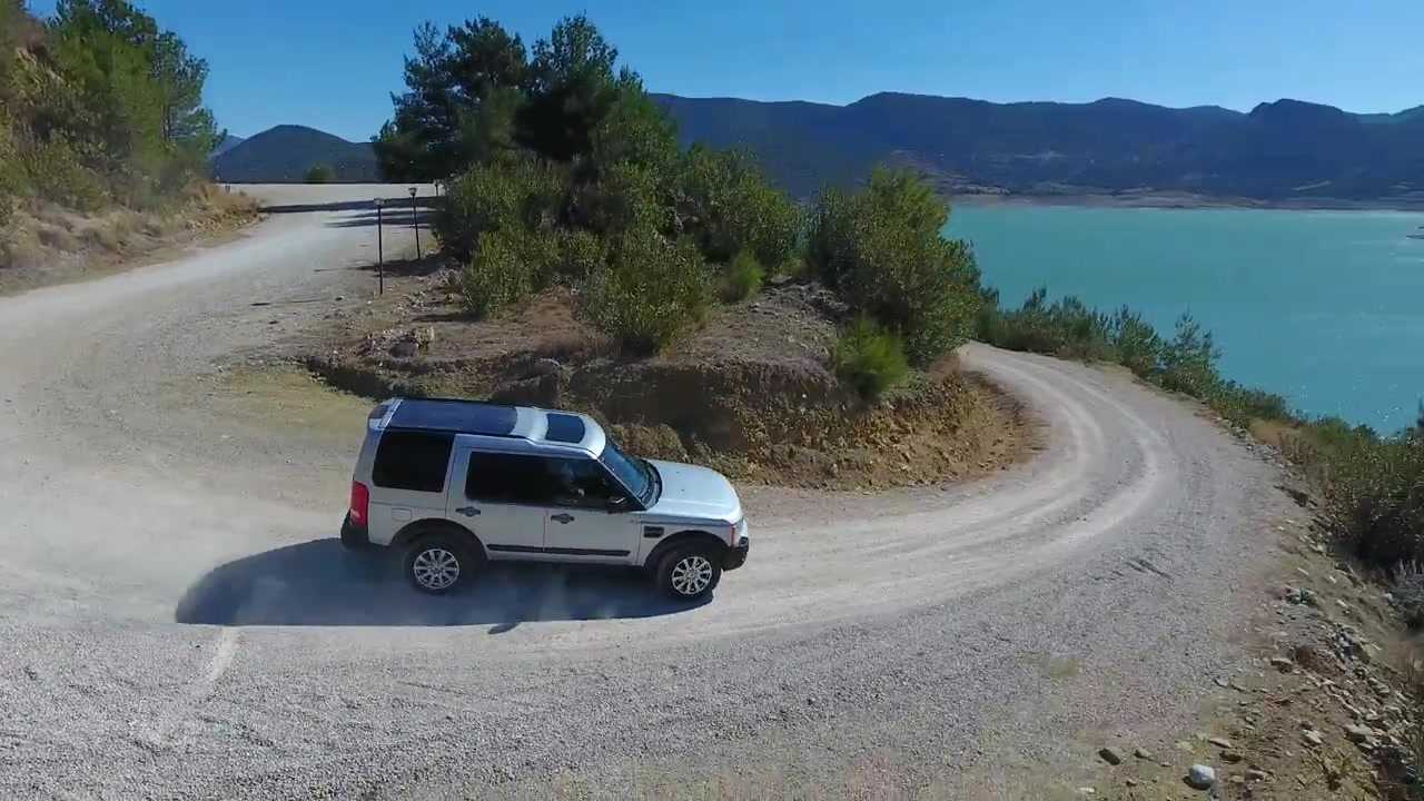 SUV argentato che guida su strada sterrata lungo un lago turchese