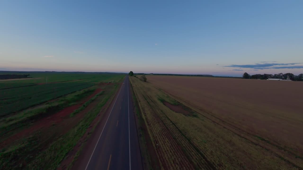 Asphalt highway crossing vast soybean plantation in Goias, Brazil, during a colorful dusk, aerial view revealing the immensity of the agricultural landscape