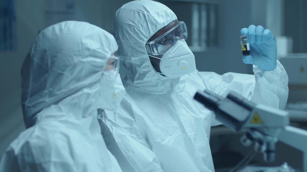 Two Scientists in Protective Uniform Discussing Blood Sample in Laboratory