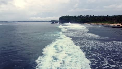 Volando-Bajo-Sobre-El-Encalado-De-Las-Olas-Del-Mar-Rompiendo-En-Una-Exuberante-Costa-Tropical