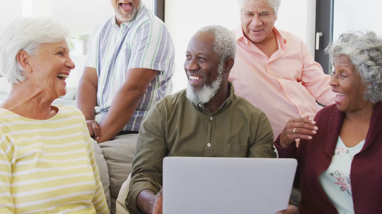Idosos felizes de diversas etnias conversando e usando um laptop em um lar de idosos.
