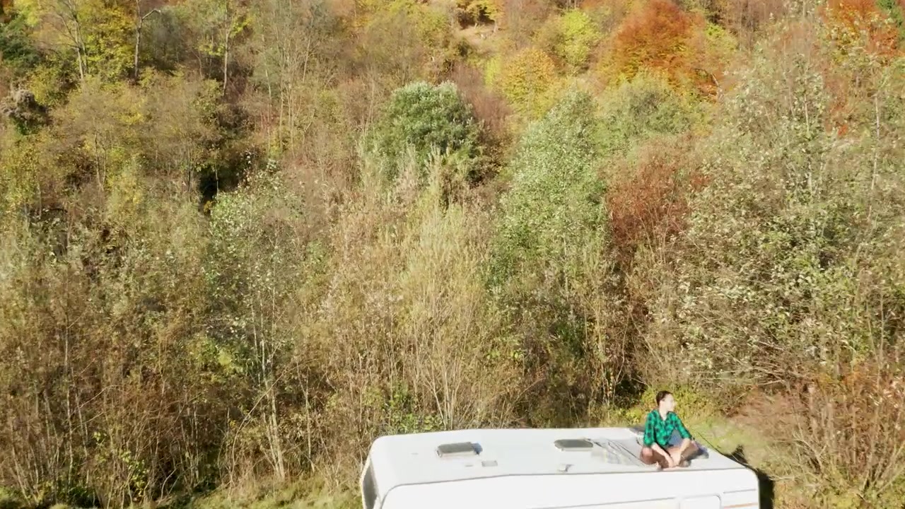 Drone passes above a woman and camper in the forest