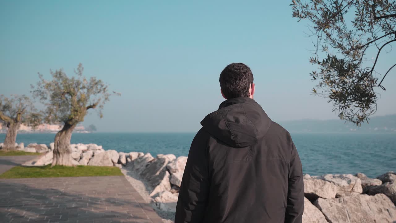 Man walking through city Salo italy, small town on lake garda. Following the promenade exploring the beautiful nature seascape and city with marina and sailboats in the background