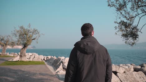 man walking through city salo italy, small town on lake garda. following the promenade exploring the beautiful nature seascape and city with marina and sailboats in the background