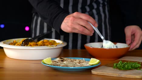 man chef making roasted cauliflower tacos: hands placing tzatziki sauce on top of tortilla to assemble the taco