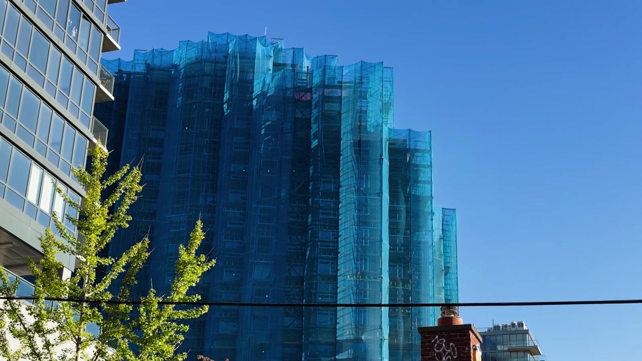 Arranha-céu em construção envolto em rede de malha azul em um dia claro