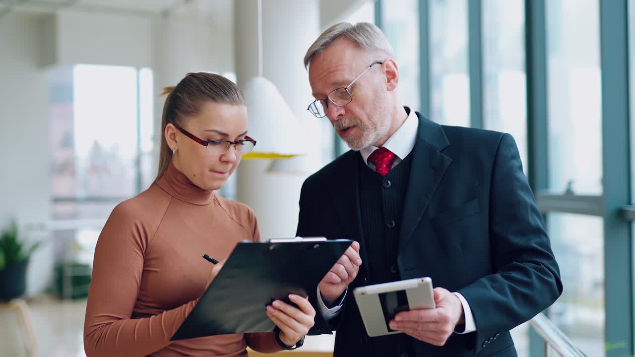 Senior man in costume and a young woman indoors. Serious businessman giving advice to his secretary in the company. Business concept.