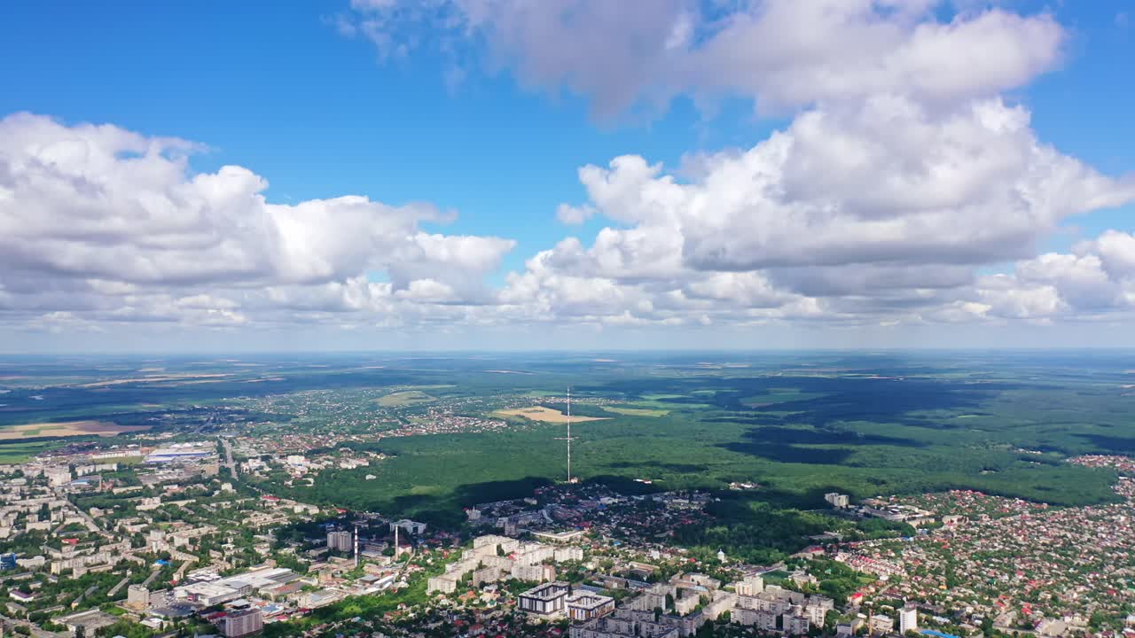 Panoramic view of a city among green nature. Cityscape under blue sky with white clouds. Beautiful scenery of a town near fields. Aerial view.