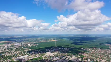 panoramic view of a city among green nature. cityscape under blue sky with white clouds. beautiful scenery of a town near fields. aerial view.