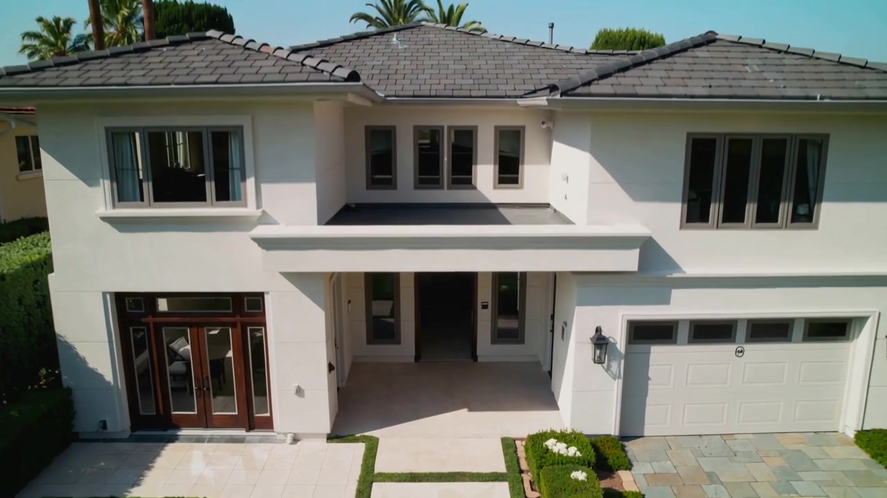 Un drone che scende rivela l'ingresso di una casa a due piani in stucco, mostrando le doppie porte e il garage.