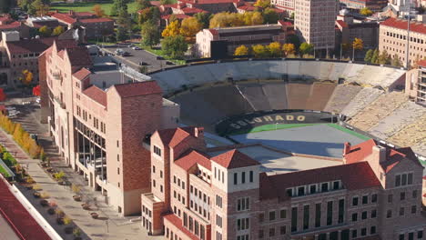 vista aérea de cerca del campus y el estadio de cuu boulder rodeado de árboles de otoño verdes y amarillos con las montañas rocosas flatiron en el fondo en la cordillera delantera de colorado