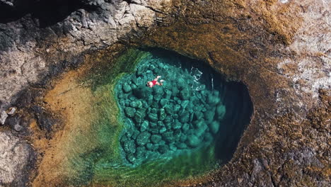 a woman in a red swimsuit is swimming in a cove near caleta de fuste