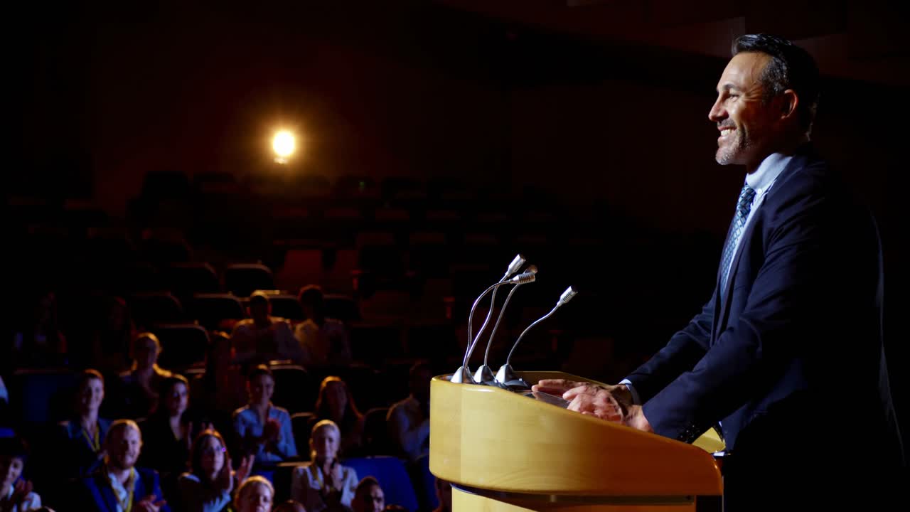 Imprenditore caucasico che parla sul palco a un seminario aziendale in auditorium 4K
