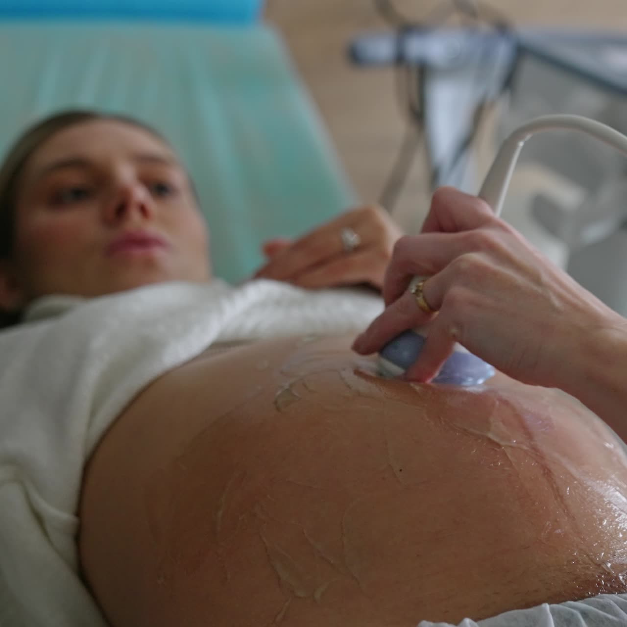 Expecting woman lies on the obstetrician's couch. Female hand moving the sensor by gelled abdomen. Close up
